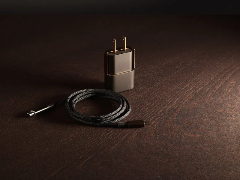 Stočený pletený kabel USB-C vedle kompaktního adaptéru na tmavém dřevěném stole.